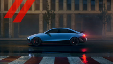 En elegant blå sportssedan er parkeret på en våd gade i byen om natten, med bygningsvinduer og røde striber i baggrunden.