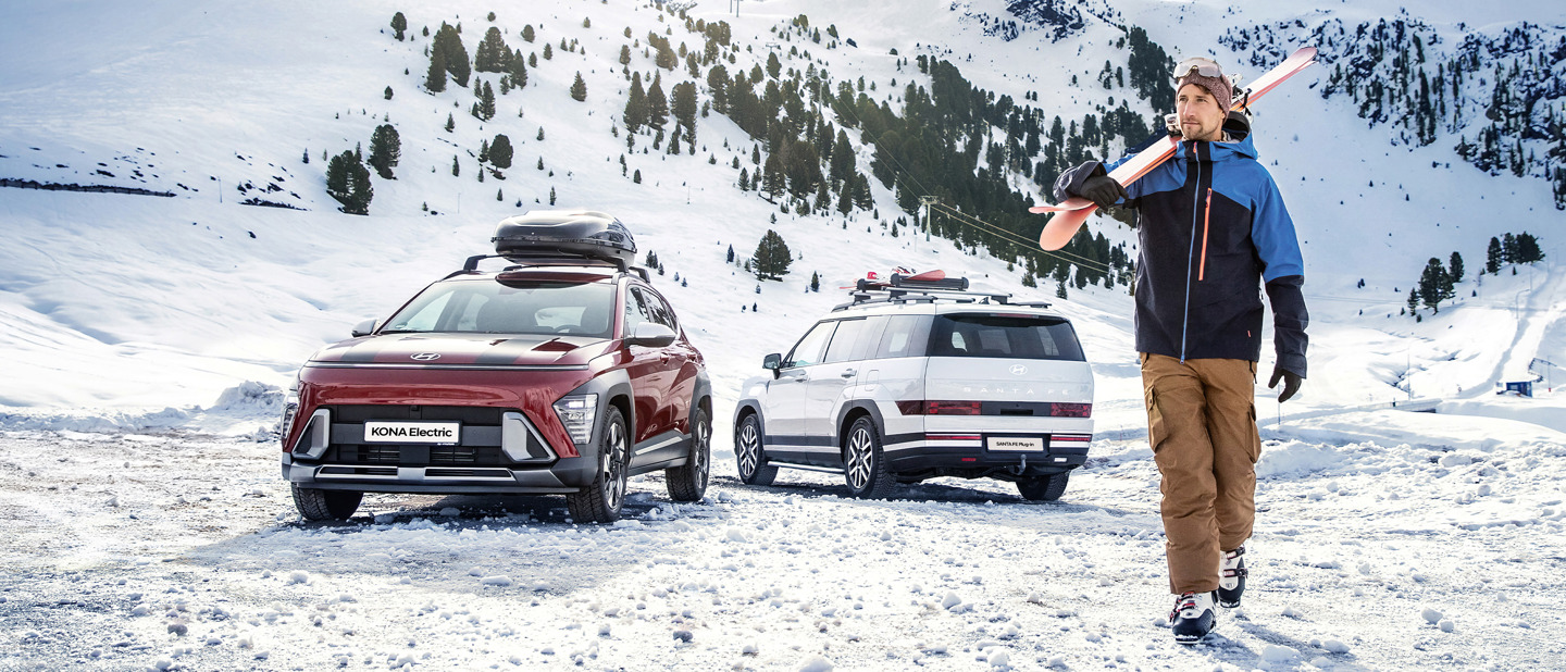 Mand går med ski forbi Hyundai KONA Electric og SANTA FE i sneklædt landskab