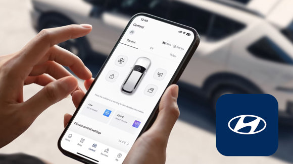 En person holder en smartphone, der viser en Hyundai-bilstyringsapp, med en parkeret Hyundai-bil og Hyundai-logo i baggrunden.