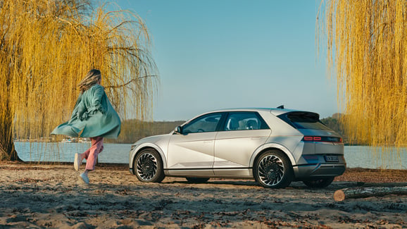 Kvinde løber mod Hyundai IONIQ 5 parkeret på strand 