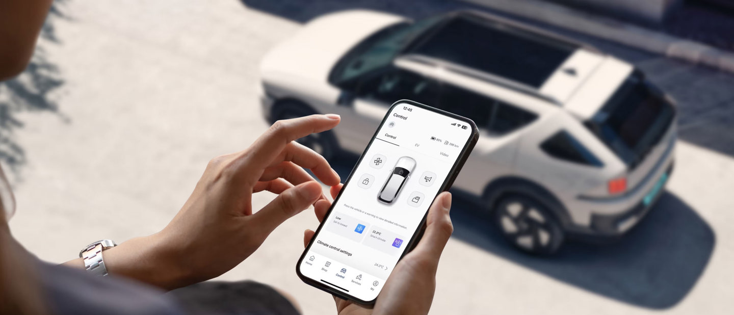En person bruger en smartphone-app til at styre eller overvåge en hvid SUV, der er parkeret på gaden.