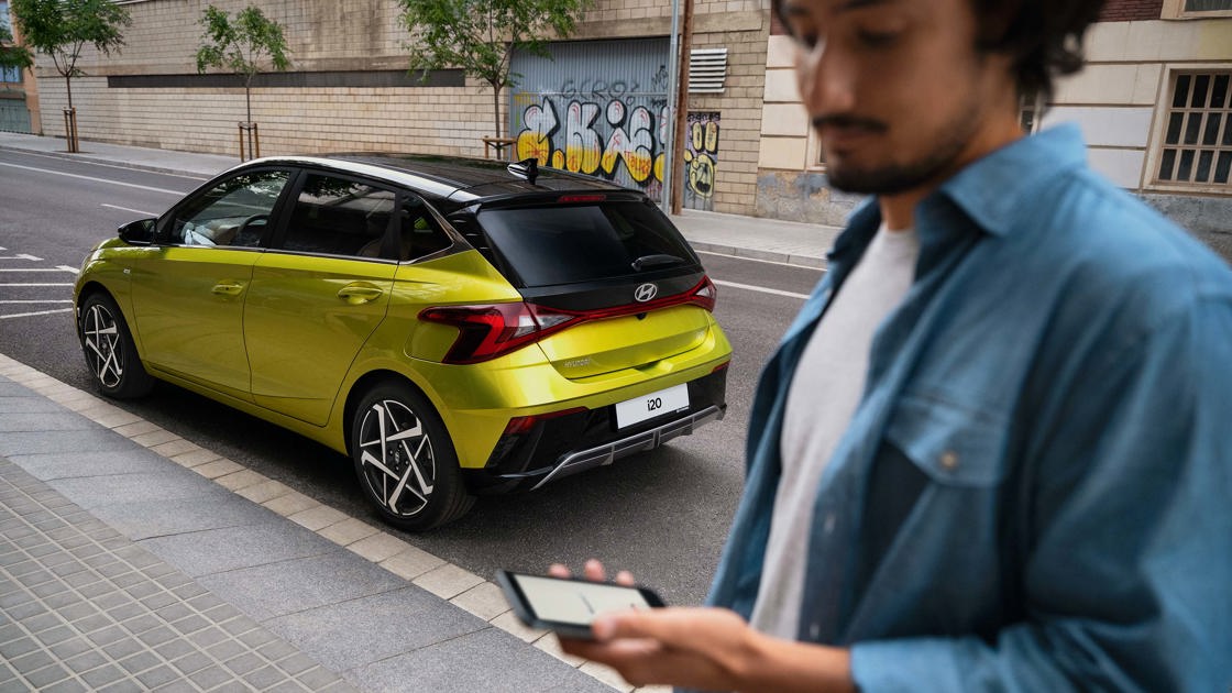 Mand står med smartphone foran parkeret Hyundai i20