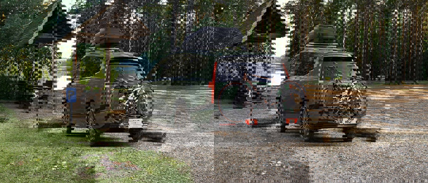 Et forvrænget, glitchet billede af to parkerede biler på en grusvej ved siden af et skovområde.