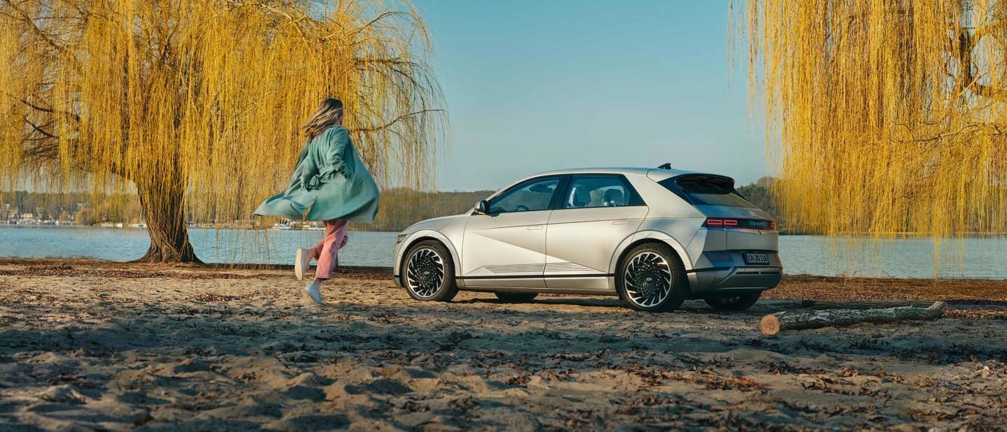 Kvinde løber mod Hyundai IONIQ 5 parkeret på strand 