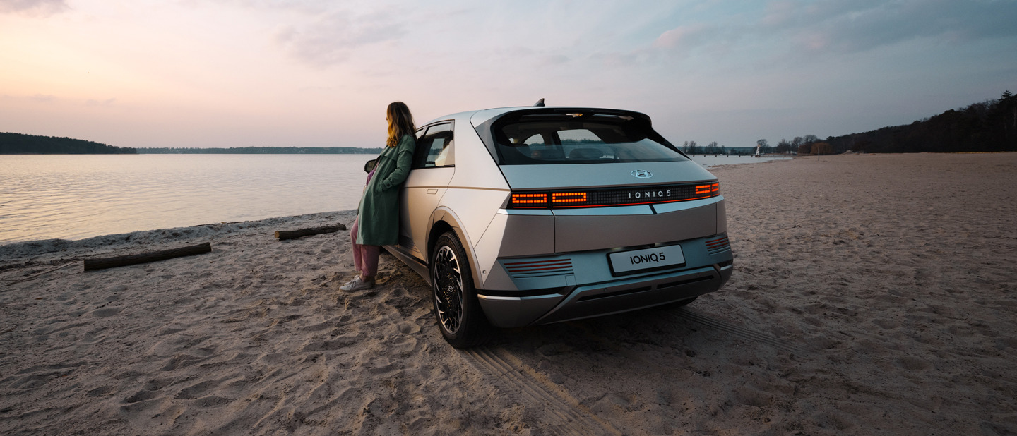 Kvinde læner sig op af Cyber Grey IONIQ 5 parkeret i sandet på en strand 