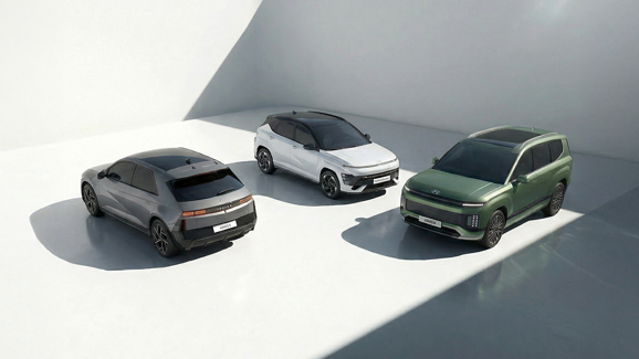 Tre moderne Hyundai-biler - en grå hatchback, en hvid SUV og en grøn SUV - er parkeret i et lyst, minimalistisk rum.
