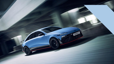 En lyseblå Hyundai Ioniq 6 elbil kører hurtigt i et moderne parkeringshus, hvor omgivelserne ser ud til at være i bevægelse.
