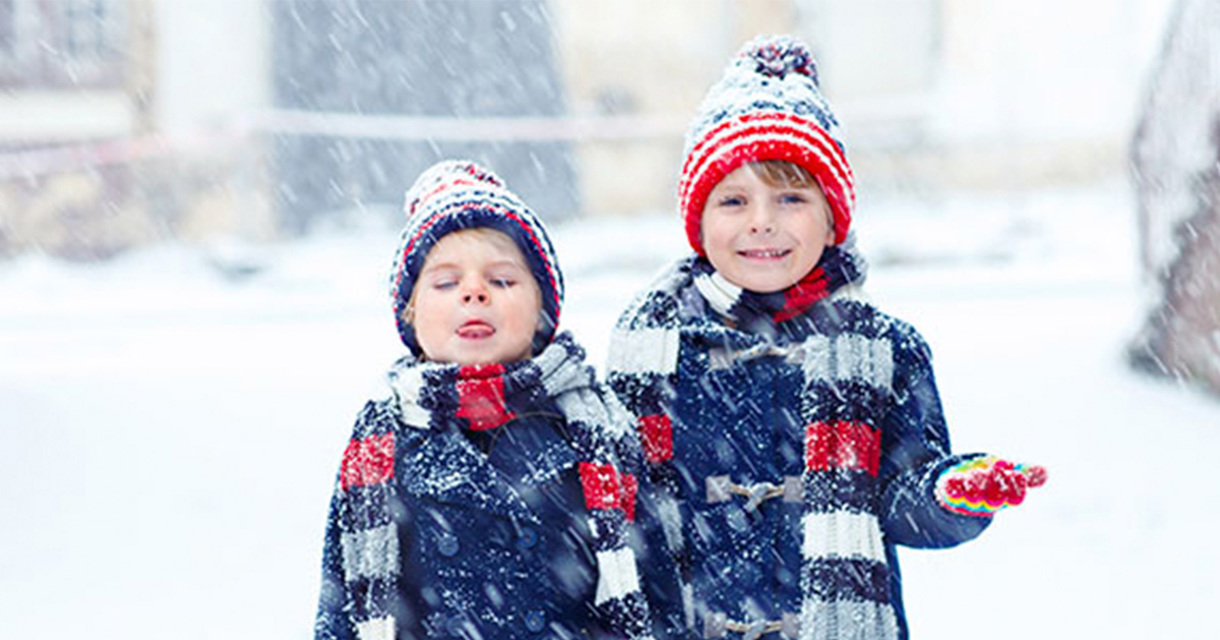 To børn iført vintertøj leger i sneen 
