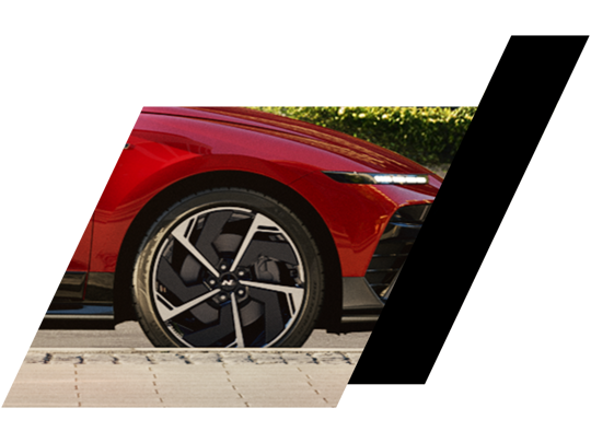 Et nærbillede af en rød bils forhjul og forlygte, indrammet af vinklede sorte og hvide grafiske former.