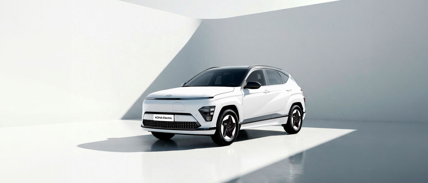 En hvid Hyundai Kona Electric SUV parkeret i et minimalt, moderne rum med hvide vægge og blød, naturlig belysning.