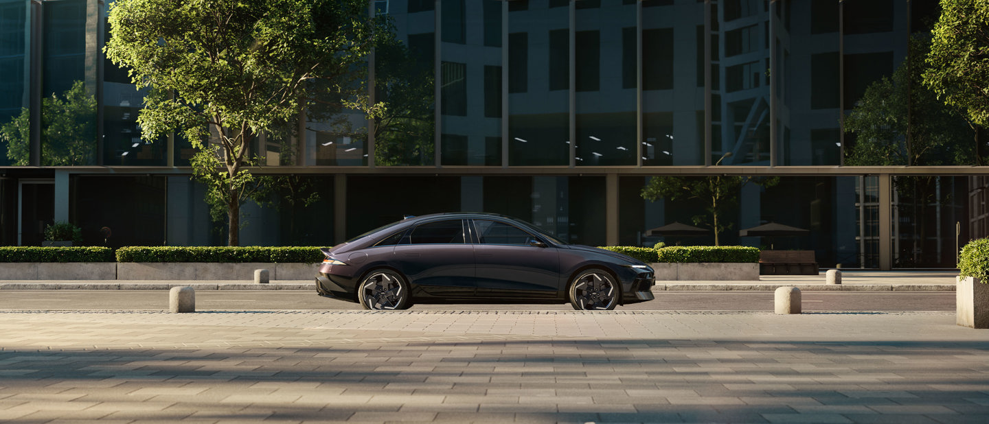 En sort sedan parkeret på en gade i byen med moderne glasbygninger og træer i baggrunden.